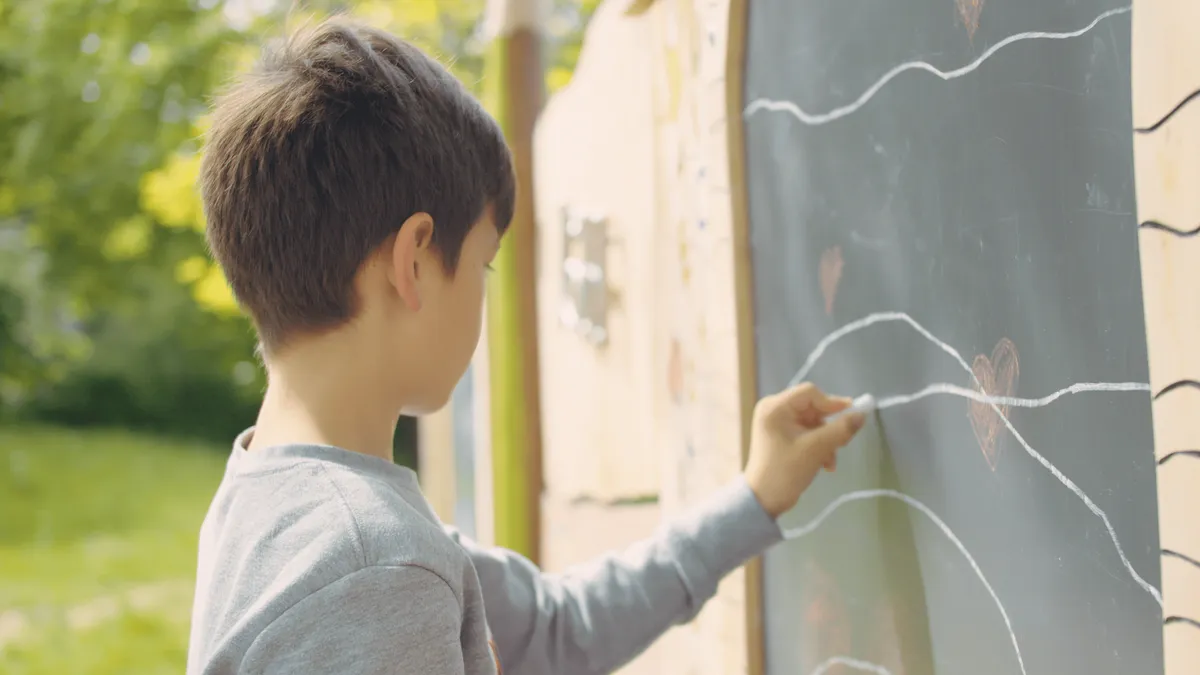 Kind zeichnet auf Tafel im Freien